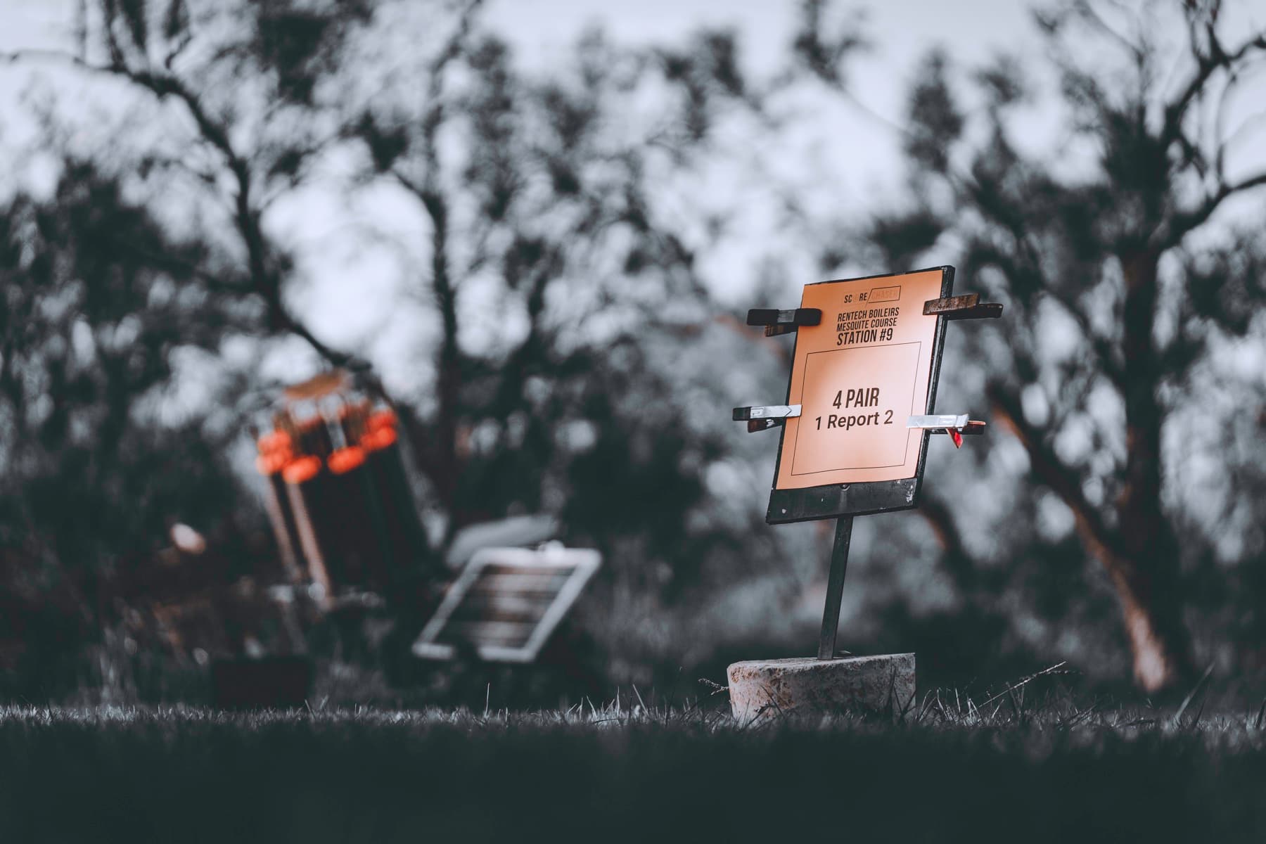 A sporting clays station sign standing low in a dark, wooded field.
