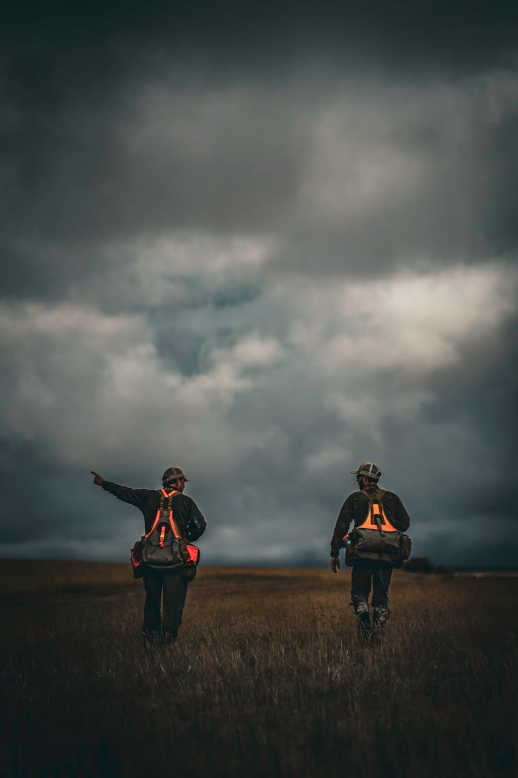 Two figures in a field below a wide stormy sky.