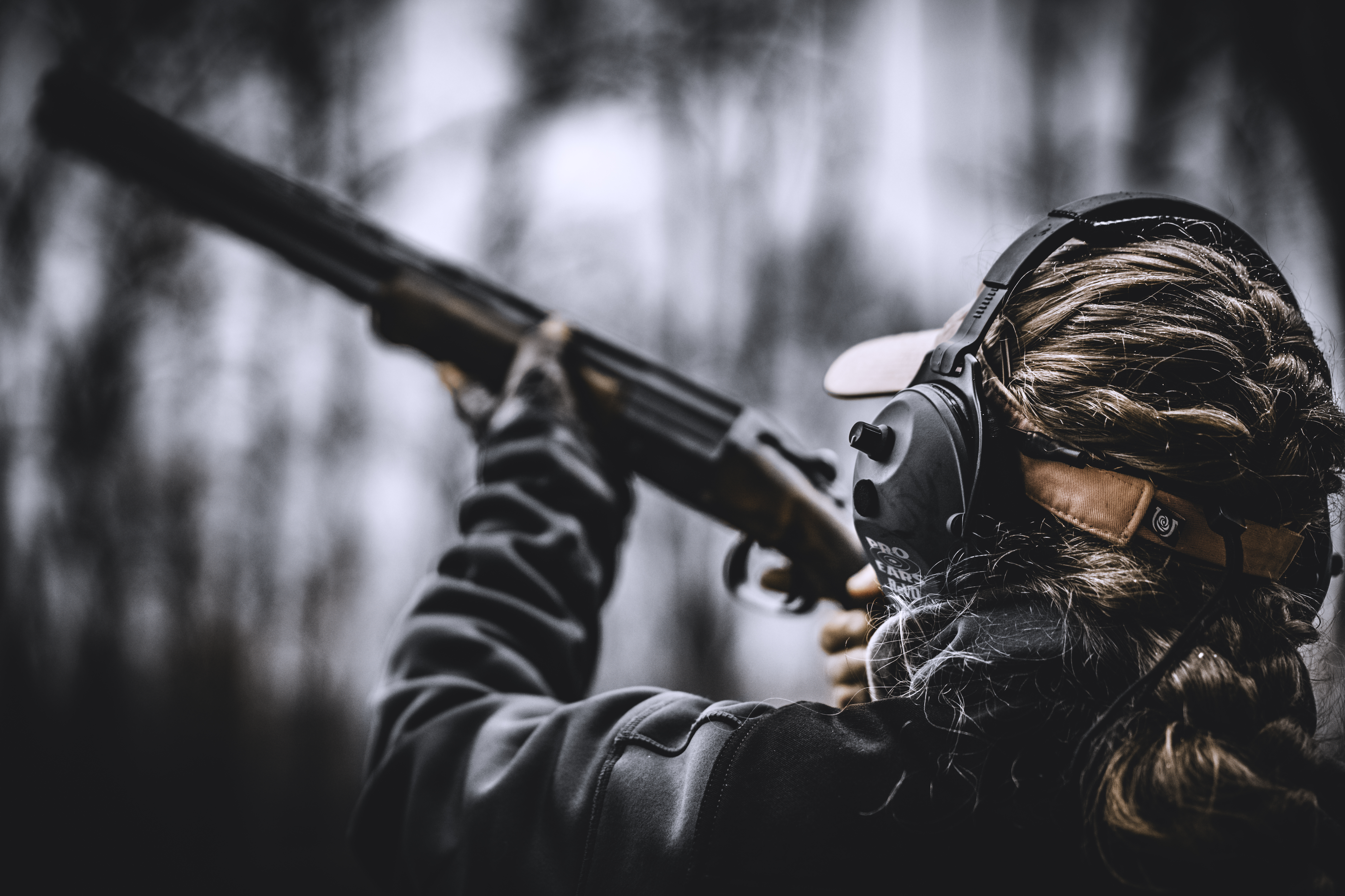 A close view from behind of a shooter raising a shotgun in a wooded field.